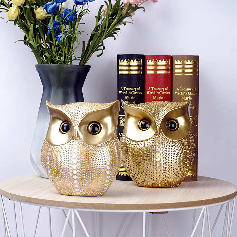Gold resin owl figurines placed on a table with books and flowers, ideal for elegant owl garden decor or patio ornamentation.